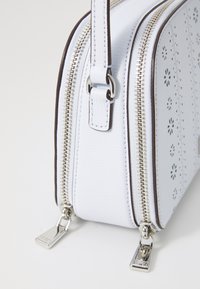 Borsa a tracolla in pelle bianca con due scomparti con zip, motivo perforato floreale, accessori in argento e tracolla regolabile.