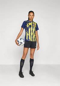 Fotbalový dres Nike s modro-žlutým pruhovaným trikem, černými šortkami, černými podkolenkami až po kolena a bílým fotbalovým míčem s modrými akcenty.