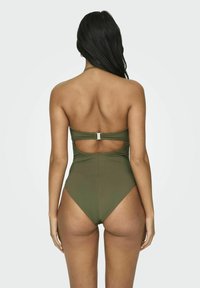 Traje de baño de una pieza en verde oliva con un diseño de espalda con corte y detalles en plata. Tejido suave y elástico con aberturas en las piernas de corte alto.