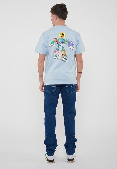 Camiseta de algodón azul claro con un gráfico colorido de un personaje en la parte posterior. Combinada con pantalones vaqueros azul oscuro y zapatillas blancas.