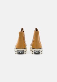 Baskets hautes en cuir marron avec une finition texturée, des coutures blanches contrastantes et une semelle en caoutchouc noir et blanc. Présente un logo en forme d'étoile.