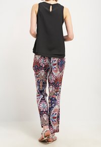 Top negro sin mangas con espalda de ojal, combinado con pantalones de estampado multicolor que presentan motivos florales y geométricos. Sandalias plateadas.