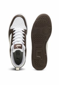 Białe i brązowe sportowe sneakersy z gładką skórzaną cholewką, perforowanym przodem, wyściełanym językiem oraz teksturowaną gumową podeszwą z logo.