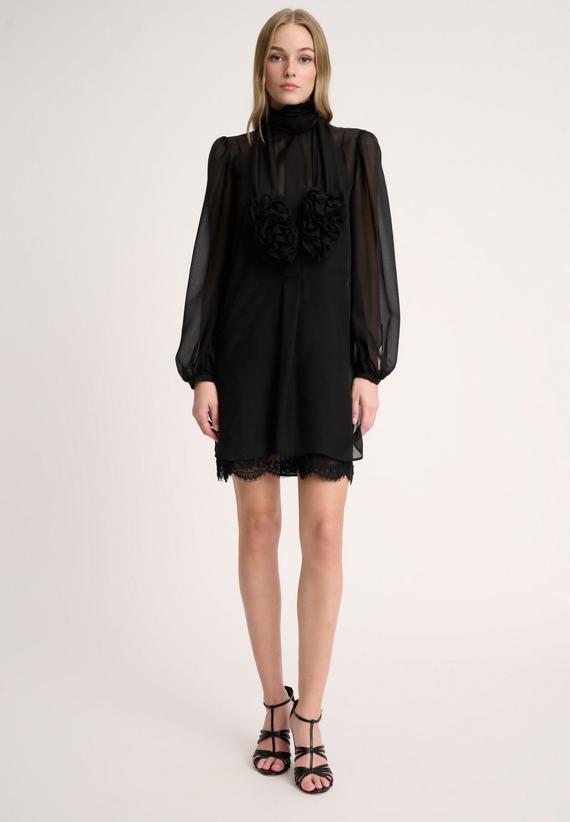 Vestido de gasa negro con mangas largas abullonadas, cuello alto y dos aplique de rosa en el cuello. Encaje en el dobladillo y textura de tela delicada.