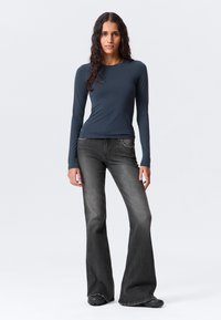 Μακρυμάνικο, εφαρμοστό μπλε σκούρο τοπ συνδυασμένο με μαύρο ξεθωριασμένο τζιν με φαρδιά μπατζάκια. Το τζιν διαθέτει μικρή μπροστινή τσέπη και ακατέργαστο τελείωμα.