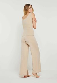Beige geripptes Tanktop mit einem runden Ausschnitt, kombiniert mit weit geschnittenen Hosen mit seitlichen Schlitzen. Weicher Stoff, lockere Passform.