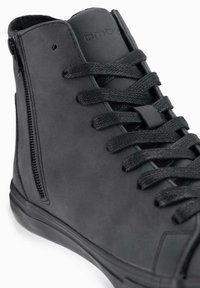 Zapatilla alta negra hecha de cuero liso con superficie texturizada, que cuenta con cordones y un zipper lateral para un fácil acceso.