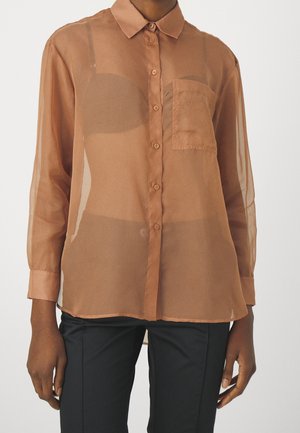 Ruskeahko läpikuultava napitettava paita, jossa on etutasku, puettuna mustan rintaliivin päälle, yhdistetty mustiin housuihin, kuvattu rinnan keskiosasta käsiin asti.