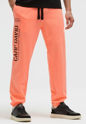 Korallenfarbene Jogginghose aus weichem Stoff, mit schwarzem Kordelzug, elastischen Bündchen und bedrucktem Schriftzug am linken Bein.