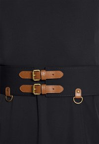 Černé látkové šaty s širokým hnědým páskem z umělé kůže, který má dvě zlaté kovové spony a zlatý kroužek. Hladká textura, přizpůsobený design.