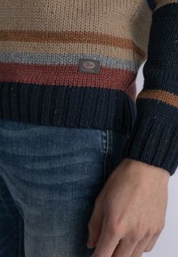 Gebreide trui met horizontale strepen in beige, roest, grijs en marineblauw. Ribgebreide manchetten en onderkant met een klein logopatch.