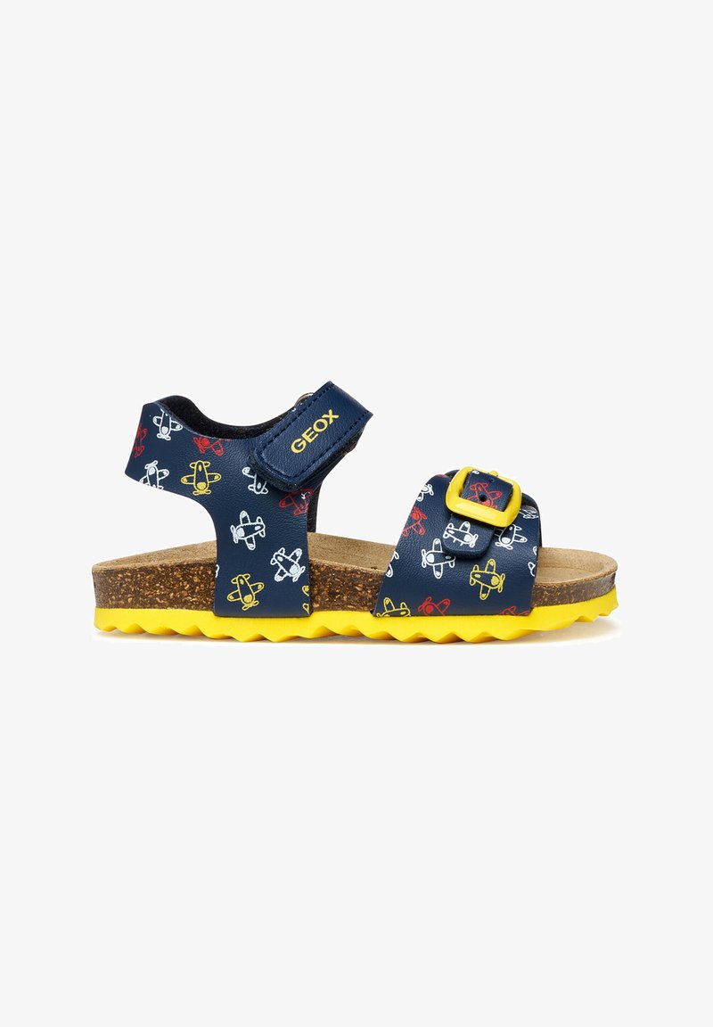 Sandale pour enfants bleu marine avec semelle jaune et motifs d'avions, équipée d'une bride ajustable et d'une boucle avec le logo "GEOX".