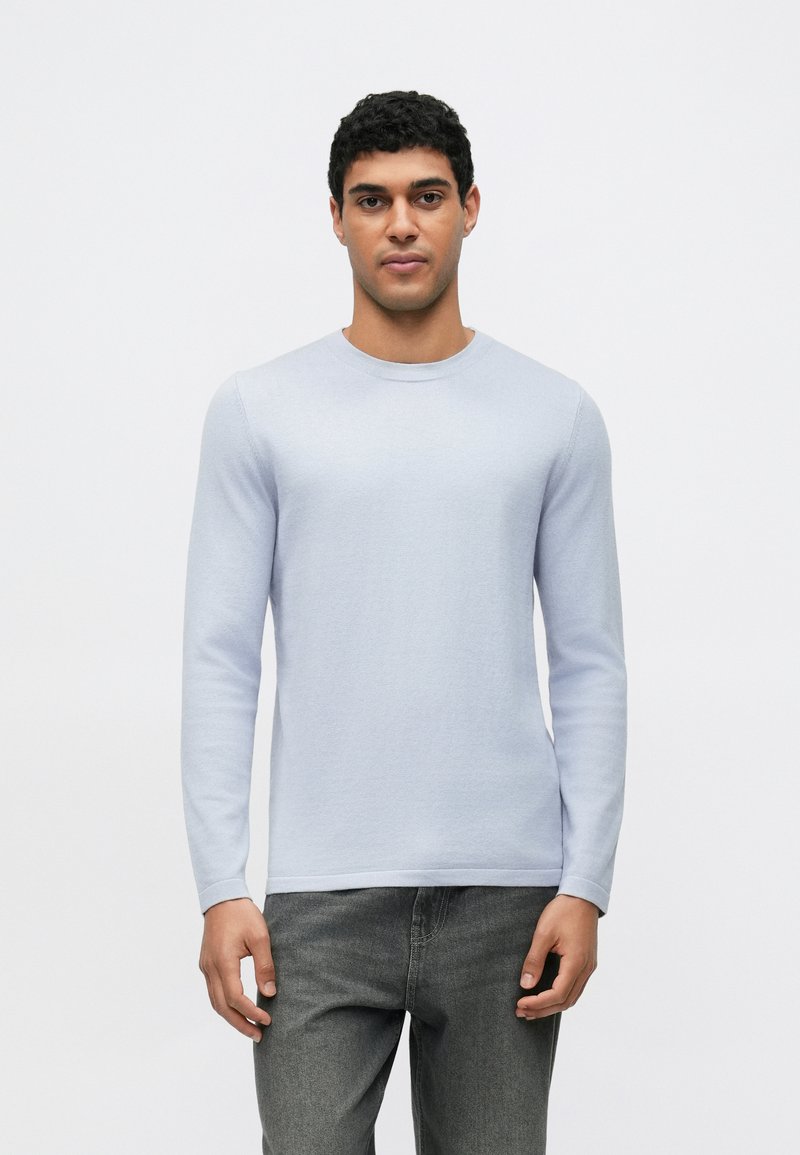 Lichtblauw shirt met lange mouwen en ronde hals, gemaakt van zacht materiaal, gecombineerd met donkergrijze jeans. Heeft een eenvoudig ontwerp en een gladde textuur.