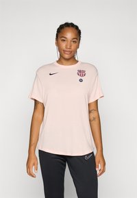 Svijetlo ružičasta, majica s kratkim rukavima od mekanog materijala, koja sadrži plavi Nike logo i grb Barcelone. Jednostavan, opušten kroj.