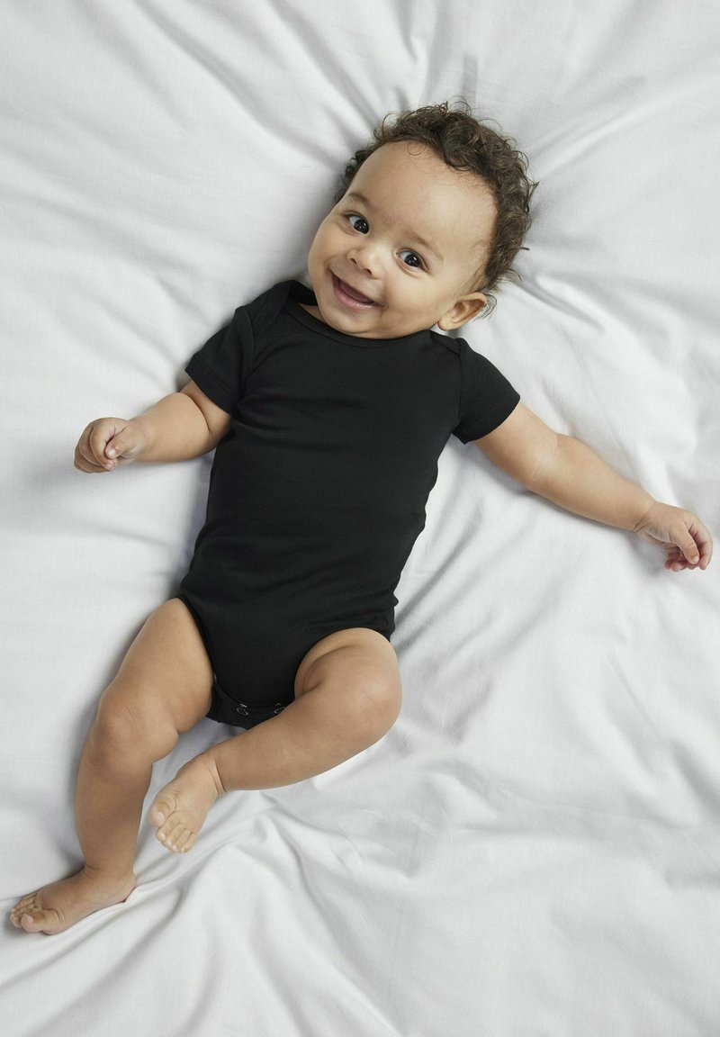 Un body de bébé noir à manches courtes sur un drap clair. Tissu en coton lisse, coupe ajustée, avec une fermeture à pression en bas. Bébé allongé avec les bras écartés.