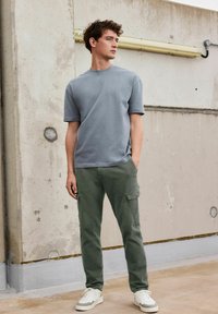 Tricou gri cu mânecă scurtă, asortat cu pantaloni cargo verzi. Ținuta are o croială lejeră, texturi subtile și adidași albi. Elemente de design simple.