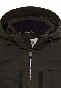 Olivgrüner Windbreaker mit Kapuze, ausgestattet mit einem Frontreißverschluss, verstellbaren Kordelzügen und einem weichen Innenfutter. Strukturierter Stoff mit schwarzen Akzenten.