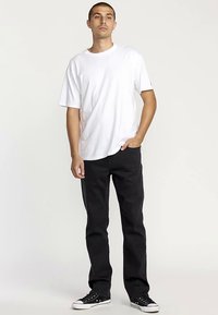 Weißes Baumwoll-T-Shirt kombiniert mit schwarzen Jeans mit geradem Bein und schwarzen Canvas-Sneakern. Das Outfit zeichnet sich durch eine lässige, entspannte Passform aus.
