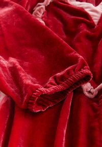 Weicher, rot samtiger Ärmel mit elastischem Bündchen, der in einer Nahaufnahme reiche Textur und Falten zeigt.