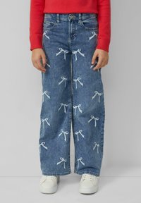 Džínové široké nohavice s bielou výšivkou mašle, s vysokým pásom, prednými vreckami a svetlomodrým pracím. Skombinované s bielymi teniskami.