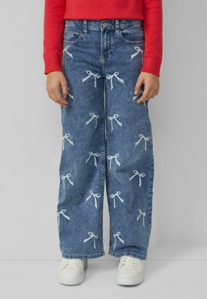 Jeans mit weitem Bein und weißer Schleifenstickerei, ausgestattet mit hoher Taille, Fronttaschen und einer hellblauen Waschung. Kombiniert mit weißen Sneakers.