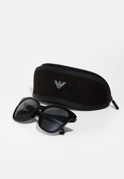 Black sunglasses with a chunky frame, dark lenses, and gold accents. Includes a black zippered case with a logo design on the front.