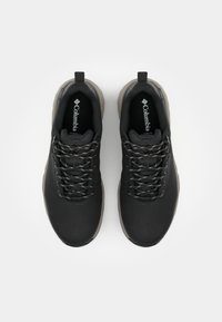 Schwarze Sportschuhe mit einer glatten Oberseite, strukturierten Akzenten, flexibler Sohle und grauen Schnürsenkeln. Markenlogo auf der Innensohle sichtbar.