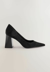 Mustasta nubukista valmistetut korkokengät, joissa on teräväreunainen kärki ja jämäkkä korko. Koron pinnassa on tekstuurinen muotoilu, joka luo elegantin ilmeen.