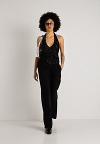 Top halter preto com detalhes texturizados, combinado com calças largas pretas. Os acessórios incluem uma bolsa prata e óculos de sol.