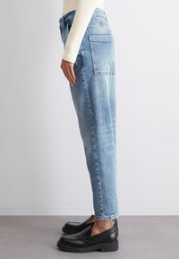 Vaaleansiniset, rentoistukkaiset farkut suoraltihaisilla lahkeilla, joissa on takataskun yksityiskohtia ja hillitty haalistuma, yhdistettynä mustiin slip-on-kenkiin.