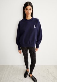 Navy sweatshirt with white ribbon logo, paired with black zebra-pattern leggings and black slip-on shoes, displayed against a light background.