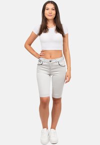 Pantaloncini di denim grigio chiaro con due tasche frontali e dettagli in cucitura più scuri, abbinati a un crop top bianco e sneakers bianche.