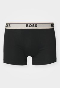 Schwarze Boxershorts aus glattem Stoff, mit einem beigen elastischen Bund, auf dem "BOSS" in Schwarz gedruckt ist. Schlichtes und enganliegendes Design.