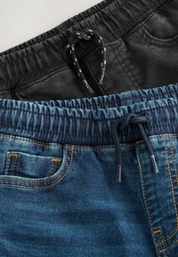 Două perechi de pantaloni sport: una neagră, cealaltă din denim bleu închis. Ambele au talie elastică cu șnur și detalii de cusătură subtile.