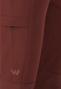 Rote Stoffhose mit einer Seitentasche und einem Logodetail in einem dunkleren Farbton. Glatte Textur und taillierte Passform.