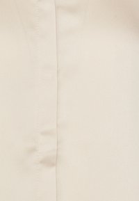 Tissu beige avec une texture lisse et un éclat subtil. Présente une couture centrale, indiquant un design sur mesure.