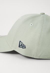 Lys grøn baseballcaps med en struktureret overflade, prydet med et marineblåt broderet logo på siden og syningsdetaljer på skyggen.