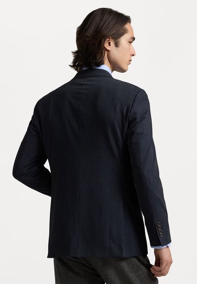 Veste de costume bleu marine foncé avec une finition texturée. Dotée de revers crantés et de deux boutons sur les poignets. Coupe ajustée pour une silhouette élégante.