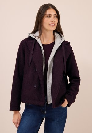Veste en polaire de couleur violet profond avec un design croisé, dotée d'une doublure à capuche grise, de poches latérales et d'une texture douce.