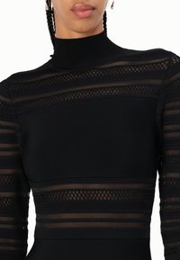 Svart langermet kjole med høy hals, med horisontale ribbede og gjennomsiktige mesh-striper som viser et teksturert design og en tettsittende form.