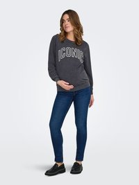 Grijze trui met ronde hals met de tekst "ICONIC", gecombineerd met donkerblauwe skinny jeans en zwarte instapschoenen. Zachte stof, casual pasvorm.