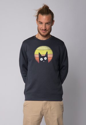 Donkerblauwe sweater van een katoenmix. Bevat een grafisch ontwerp van een zwarte kat binnen een meerkleurige zonsondergangcirkel. Ribgebreide manchetten en zoom.
