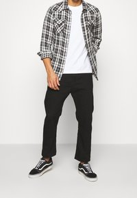 Černobílá kostkovaná košile přes bílý tričko, spárovaná s černými kalhotami a černými teniskami. Vlastnosti: zapínání na knoflíky, dlouhé rukávy.