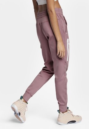 Lyserøde joggers med en slim fit-design, der har en hvid lynlåslomme, ribbede manchetter og sidelommer. Båret med beige sneakers.