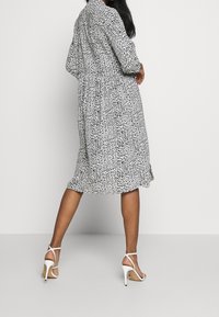 Abito midi a fantasia bianco e nero con vita cintrata, maniche lunghe e gonna fluida. Abbinato a tacchi alti bianchi con cinturini.