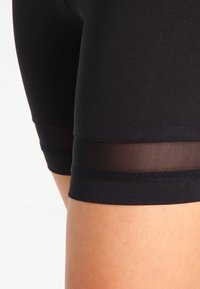 Mustat urheilushortsit, joissa on sileä kangas, ja joissa on läpinäkyvä verkkonauha alareunassa sekä mukava, istuva malli.