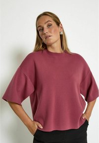 Pink, oversized sweater with short sleeves and a high neckline. Soft texture and a relaxed fit, featuring a straight hem and minimal design details.