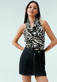 Haut à col boule en imprimé zèbre noir et blanc, associé à une mini-jupe en denim foncé avec fermeture éclair et bouton à l'avant.