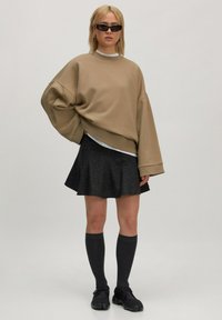 Overmaatse beige sweater met verlaagde schouders, laagjes over een wit shirt. Zwarte uitlopende rok met zilveren spikkels, knie-hoge donkere sokken en zwarte schoenen.