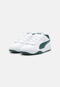 Des chaussures de sport blanches en matériau synthétique avec des accents verts, présentant un design bas, un bout arrondi et une semelle en caoutchouc plate.